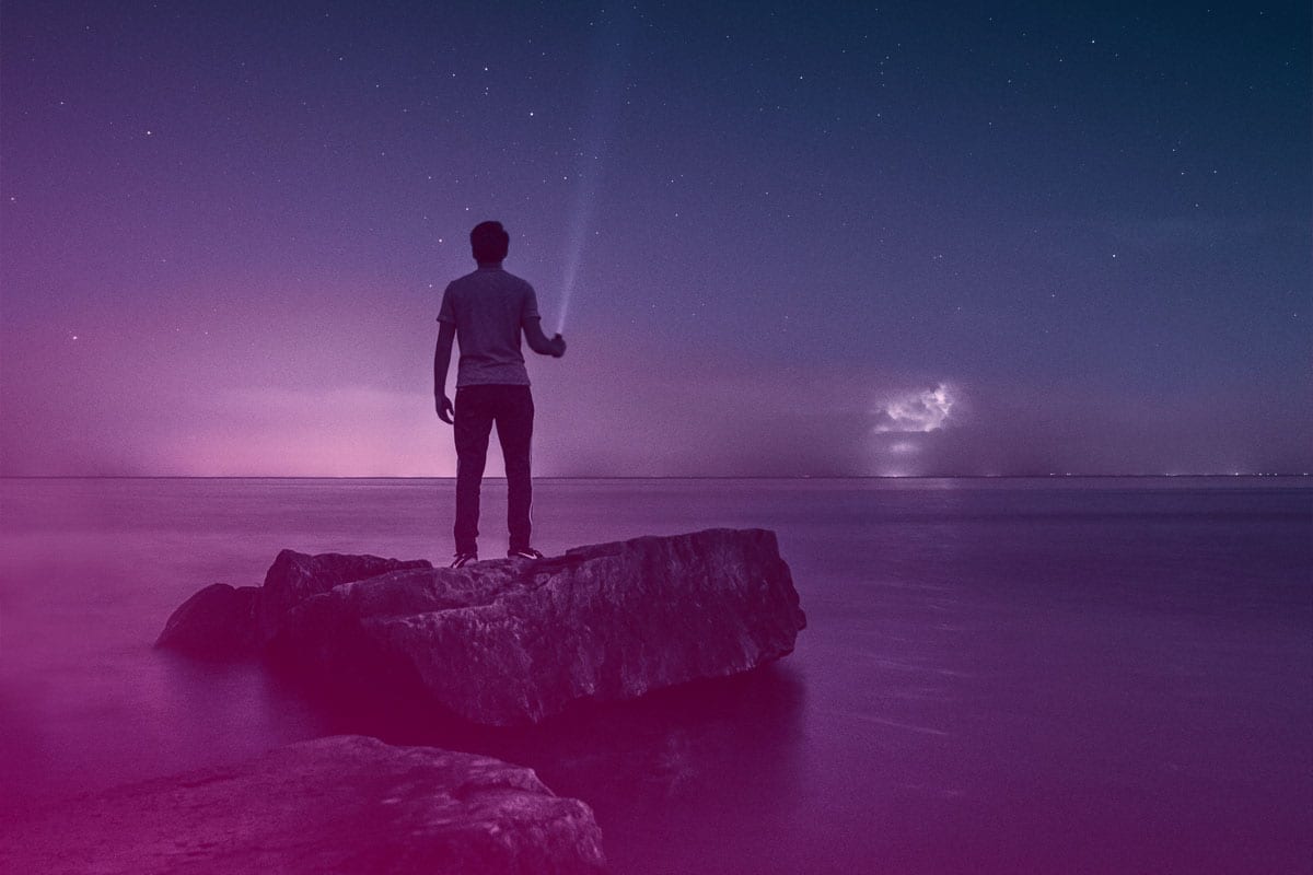 a man holding a flashlight standing on a rock overlooking the sea at dusk