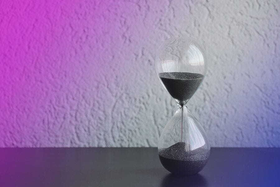 A sand hourglass sitting on a table in front of a colorful background, representing time and visual aesthetics for a website design agency.